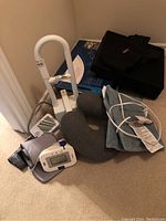 Photo showing the adjustable bedside handrail, neck pillow, heating pad, wedge pillow, back support cushion, and two blood pressure monitors with arm cuffs on the floor.