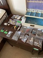 Full view of jewelry box open with assorted jewelry laid out on table in bags, including brooches, pendants, and sewing kit