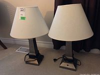 Pair of matching metal base table lamps with white fabric shades shown together on the floor.