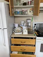 Photo showing kitchen counter with Pyrex and Corningware casserole dishes stacked, a white Brita filter pitcher, an electric kettle, kitchen timer scale, and other small kitchen appliances and items on and around the countertop and shelving.