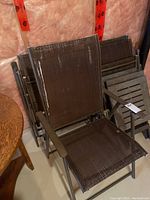 Four brown outdoor lawn chairs with mesh fabric stacked together along with three small brown plastic tables with slatted tops. Chairs have metal frames, mesh seat and back, with visible wear and some staining.
