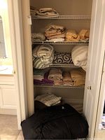 Closet shelf with folded assorted bed linens and towels in beige, cream, purple, and patterned designs.