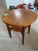 Full view of round mid century modern wooden end table showing legs and lower shelf.