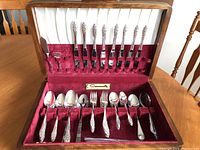 Partial view of flatware set including knives, forks, spoons, and serving pieces organized in the velvet lined canteen box showing the detailed ornate handles.