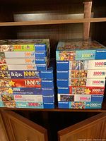 Two stacks of Ravensburger puzzle boxes on wooden shelving