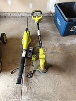 Photo showing Ryobi leaf blower (left), string trimmer (right), charger and line spools on concrete floor.