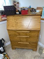 Front view of the softwood secretary desk showing the drop-front door and three drawers with wooden handles.