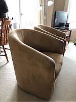 Pair of tan microsuede swivel tub chairs showing the curved back and seats, with noticeable wear and discoloration on the arms.
