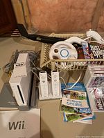 Wide shot showing console, two Wii controllers, steering wheel attachment, games in basket, and manuals on floor.