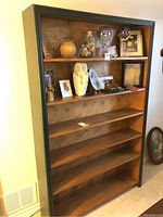 Front view of tall solid wood bookcase showing natural wood shelves with decorative items placed on top shelf and frame painted dark green.