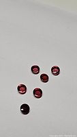 Photo of seven small round cabochon Rhodolite garnet gemstones on white background showing deep pink, purple and red tones