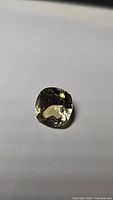 Photo of a single bright lemon yellow cushion cut citrine gemstone placed on a white background, showing its facets and clarity.