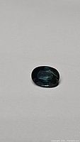 Oval cut blue sapphire with teal undertone on a plain background showing gemstone color and cut.
