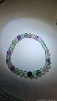 Fluorite bracelet composed of multi-color polished round beads, displayed in a circular shape on a plain background under light.