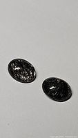 Pair of oval cabochon black rutilated quartz gemstones with black tourmaline inclusions, shown on white background, highlighting the needle-like inclusions in each stone.