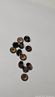 Top view of 14 calibrated round cut Smokey Quartz stones scattered on white background.