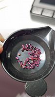 Parcel of small round purple garnet cabochons in a black weighing dish, showing size and quantity.