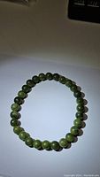 Photo showing a circular stretchy bracelet made of round green jade beads on a white surface.