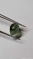 Close-up image of pear-shaped green tourmaline held with tweezers showing natural inclusions and transparency.