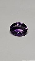Single oval cut purple amethyst gemstone with high luster and strong color shown on a neutral background.