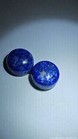 Photo of two round natural lapis lazuli cabochon gemstones showing deep blue color with golden flecks under lighting.