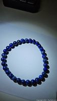 Photo of a deep dark blue Lapis Lazuli beaded stretchy bracelet laid out in a circular shape on a white surface.