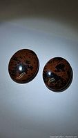 Two polished oval mahogany jasper cabochon stones with reddish-brown and black speckled patterns.