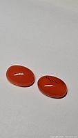 Pair of bright mandarin orange oval cabochon carnelian gemstones on white background, showing smooth polished surface and natural inclusions.