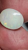 Close-up image of an oval polished Ethiopian opal held between fingers, showing white translucent body with flashes of color