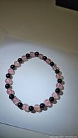 Photo of circular stretchy bracelet made with natural black onyx and pink strawberry quartz beads placed on white background.