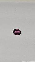 Oval cut purple-pink sapphire gemstone photographed on neutral background showing color and clarity.