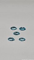 Five marquise-cut paraiba blue apatite gemstones arranged on a plain surface showing facets and bright blue color.