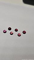 Seven natural rhodolite garnet gemstones on white background showing pink-red hues and transparency.