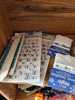 Photo of several sheets of alphabet rubber stamps with different fonts along with two unopened packs of Wright's Classic Snowflake cotton swabs on a wooden surface.