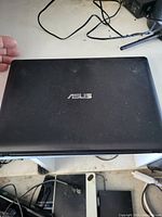 Closed black ASUS laptop with textured lid and visible light surface wear, top ASUS logo present.