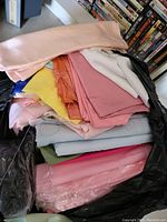 Photo showing multiple folded linen fabric pieces in varying pastel and bright shades stacked inside a black plastic bag.