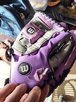 Close-up photo of a purple Wilson baseball glove showing the logo, wrist strap, and finger slots.