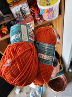 Photo showing two brand new orange yarn skeins with original labels intact.