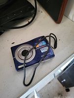 Blue Olympus compact digital camera with wrist strap, showing front and lens area.