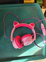 Pink cat ear headphones with wired connection placed on a teal surface.