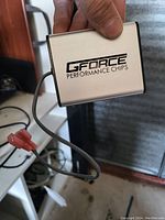 Handheld GForce Performance Chip device showing front with logo, attached wire, and red connector.