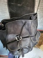 Close-up photo showing front and side view of dark brown leather knapsack, highlighting top flap and front buckle pockets.