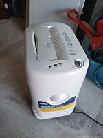 Photo of a white Royal brand paper shredder, showing the top with controls and paper slot, and the bottom waste bin, placed in a garage setting.