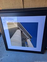 Framed photo showing two classical columns from below against clear blue sky, in black frame with white matting.