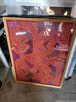 Photo of a framed abstract geometric artwork with red, orange, and purple maze-like designs.