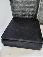 Photo of a dusty black Sony PlayStation 4 console with minor surface marks, no power cord included.