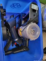 Portable handheld vacuum cleaner with transparent dust container and power button visible, lying inside a blue bin.