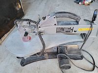 Side view of gray and black scroll saw showing handle, arm, blade guard, and base with power cord.