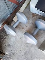 Two silver hexagonal dumbbells placed on a concrete floor, showing slight wear and use marks.