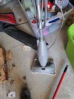 Full view of the Shark steam mop cleaner standing upright on a concrete floor with surrounding storage bins and other items.